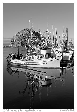 Fishing boats reflected in harbor,  and Morro Rock, early morning. Morro Bay, USA (black and white)