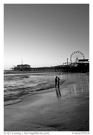 Couple standing on the beach at sunset, with pier and Ferris Wheel behind. Santa Monica, Los Angeles, California, USA