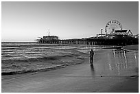 Couple reflected in wet sand at sunset, with pier and Ferris Wheel behind. Santa Monica, Los Angeles, California, USA ( black and white)