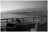 Two women sitting on bench at sunset , Santa Monica Pier. Santa Monica, Los Angeles, California, USA (black and white)