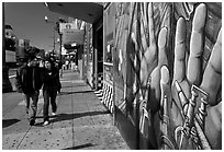 Couple walks past mural on Mission street, Mission District. San Francisco, California, USA (black and white)