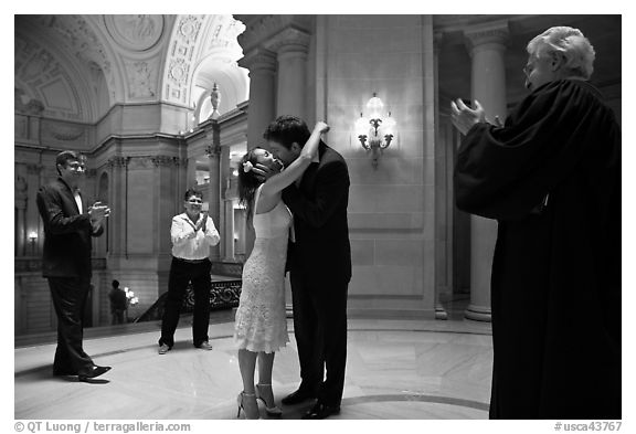 Just married couple kissing, witness and officiant applauding, City Hall. San Francisco, California, USA (black and white)