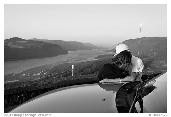 Couple embracing on car hood, with view of mouth of river gorge. Columbia River Gorge, Oregon, USA (black and white)