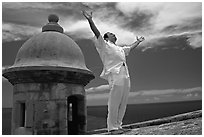 Man standing next to a lookout turret, with arms spread, El Morro Fortress. San Juan, Puerto Rico ( black and white)