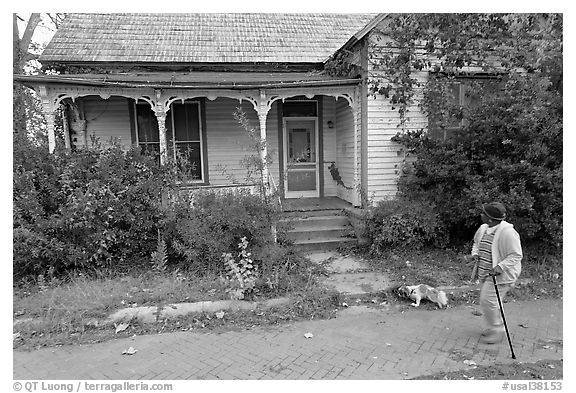 Woman walking dog in front of a crooked house. Selma, Alabama, USA (black and white)