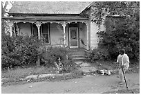 Woman walking dog in front of a crooked house. Selma, Alabama, USA (black and white)