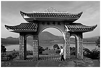 Pagoda gate with woman standing near lake. Da Lat, Vietnam (black and white)
