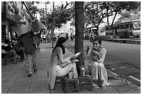 Women elegantly dressed in ao dai eating on the street. Ho Chi Minh City, Vietnam (black and white)