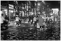 Traffic passes man pushing food cart on flooded street at night. Ho Chi Minh City, Vietnam (black and white)