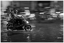 Couple sharing fast night ride on wet street. Ho Chi Minh City, Vietnam (black and white)