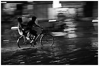Men sharing bicycle ride at night on wet street. Ho Chi Minh City, Vietnam (black and white)
