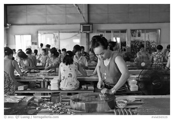 Woman cutting strips of coconut candy in factory. Ben Tre, Vietnam (black and white)