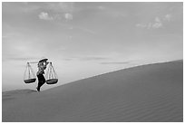 Woman with yoke baskets walks on sand dunes. Mui Ne, Vietnam (black and white)