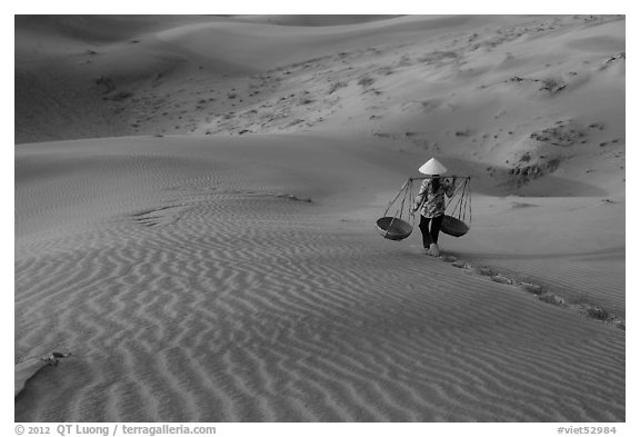 Woman with conical hat carries pannier baskets. Mui Ne, Vietnam (black and white)