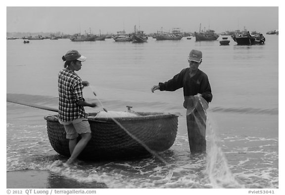 Man and woman gathering fishing net onto roundboat. Mui Ne, Vietnam (black and white)