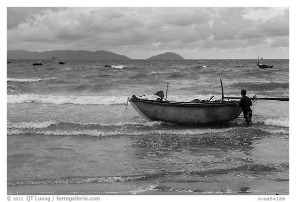 Man entering ocean with boat in stormy weather. Da Nang, Vietnam
