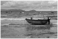 Man entering ocean with boat in stormy weather. Da Nang, Vietnam (black and white)