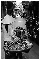 Woman pushing bicycle loaded with vegetable for sale in narrow street, old quarter. Hanoi, Vietnam (black and white)
