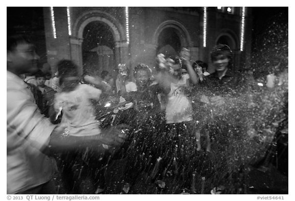 Revellers celebrating with spray in front of Notre Dame Cathedral on Christmas Eve. Ho Chi Minh City, Vietnam (black and white)