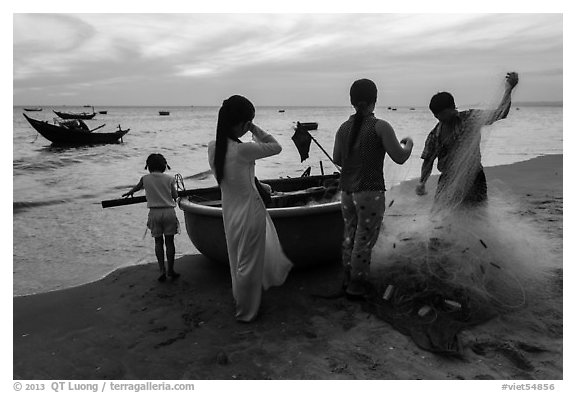 Fishermen folding net out of coracle boat as children watch. Mui Ne, Vietnam (black and white)