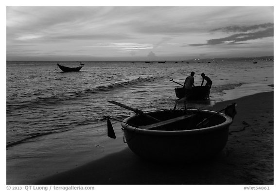 Fishermen bringing round coracle boat to shore at sunset. Mui Ne, Vietnam (black and white)