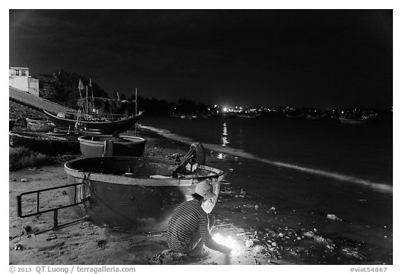 Man with fire next to coracle boat at night. Mui Ne, Vietnam (black and white)