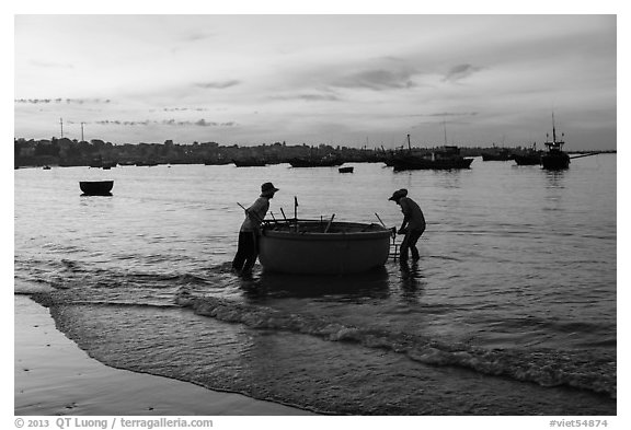 Fishermen pushing coracle boat at dawn. Mui Ne, Vietnam (black and white)