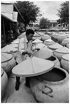 Man lifting covers of jars with fermented fish sauce. Mui Ne, Vietnam (black and white)
