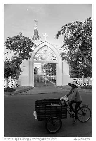 Woman bicycling in front of church. Tra Vinh, Vietnam (black and white)