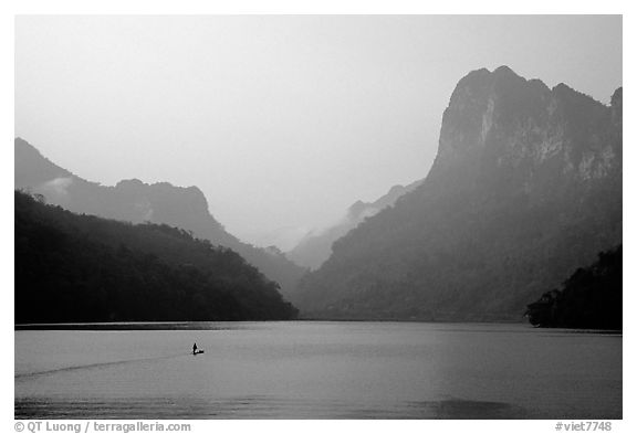 Dugout boat in Ba Be Lake, surrounded by tall cliffs, early morning. Northeast Vietnam (black and white)