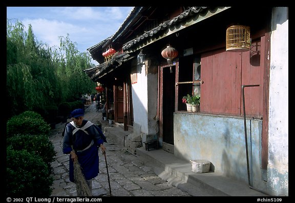 Naxi woman sweeps the floor at the door of her wooden house. Lijiang, Yunnan, China