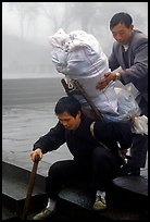 Porter getting helped to shoulder a heavy load on a back frame. Emei Shan, Sichuan, China (color)
