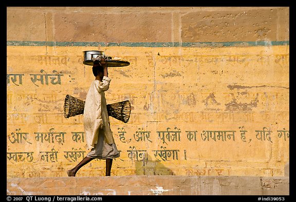 Man carrying a plater in front of wall with inscriptions in Hindi. Varanasi, Uttar Pradesh, India (color)
