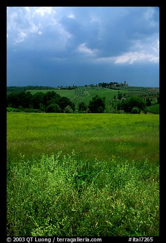 Field and distant village under storm skies. Tuscany, Italy