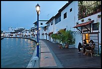 Women relaxing in front of riverside house, dusk. Malacca City, Malaysia