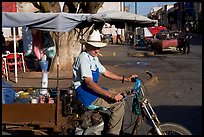 Man with cigarette riding a motorcycle-powered food stand on town plaza. Mexico (color)