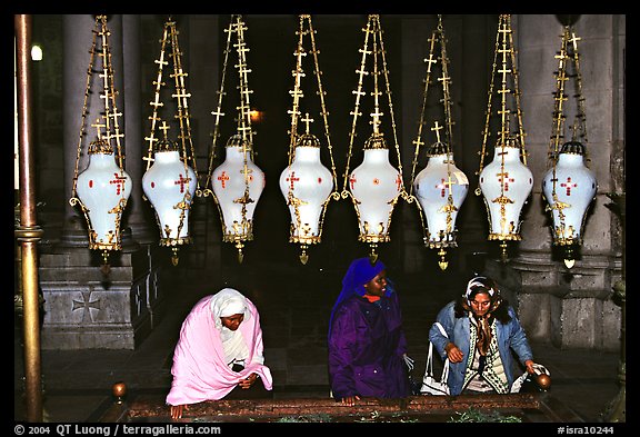 Women worshiping beneath hanging lamps inside the Church of the Holy Sepulchre. Jerusalem, Israel (color)