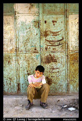 Young boy sitting in front of a closed store, Hebron. West Bank, Occupied Territories (Israel)