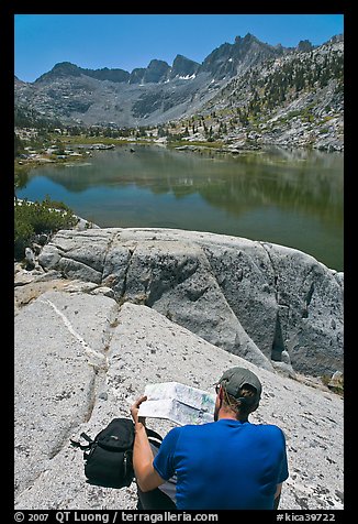 Hiker looking at map in front of lake, lower Dusy Basin. Kings Canyon National Park, California