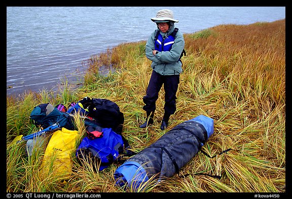 Canoeist standing next to gear and deflated and folded  canoe. Kobuk Valley National Park, Alaska (color)
