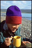 Backpacker drinking from a cup, with mosquitoes on her hat. Lake Clark National Park, Alaska