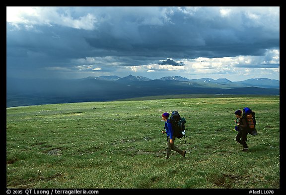 Two backpackers seen from the side walking fast in the tundra. Lake Clark National Park, Alaska