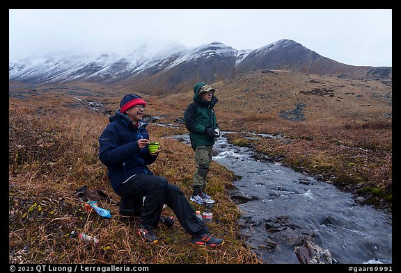Backpackers eating by a creek and snowy mountains. Gates of the Arctic National Park (color)