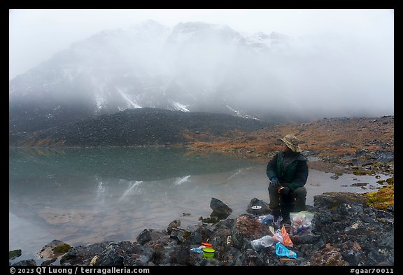 Backpacker eating near lake with foggy mountain. Gates of the Arctic National Park (color)