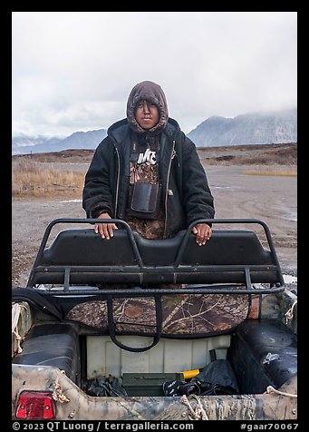 Nuamiunt boy standing on all-terrain vehicle, Anaktuvuk Pass Airport. Gates of the Arctic National Park (color)