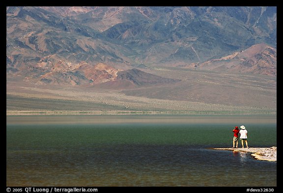 Two tourists on shore of rare lake on the floor of the Valley. Death Valley National Park, California, USA.