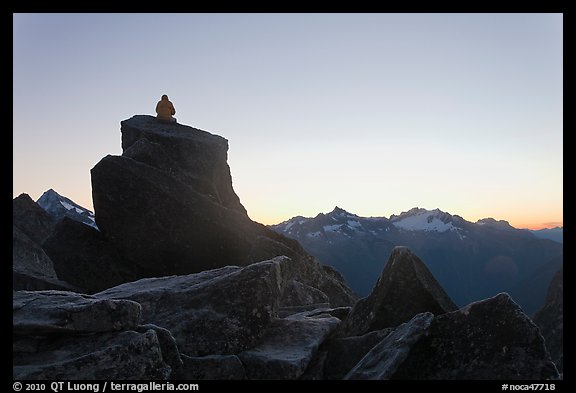 Man sitting on rock contemplates mountains at sunrise, North Cascades National Park. Washington, USA.