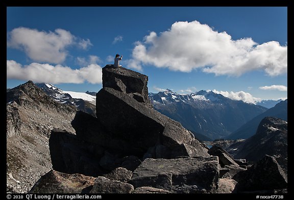 Man sitting on rock photographs mountain panorama, North Cascades National Park. Washington, USA.