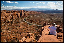 Tourist taking picture from top of fin. Arches National Park, Utah, USA.