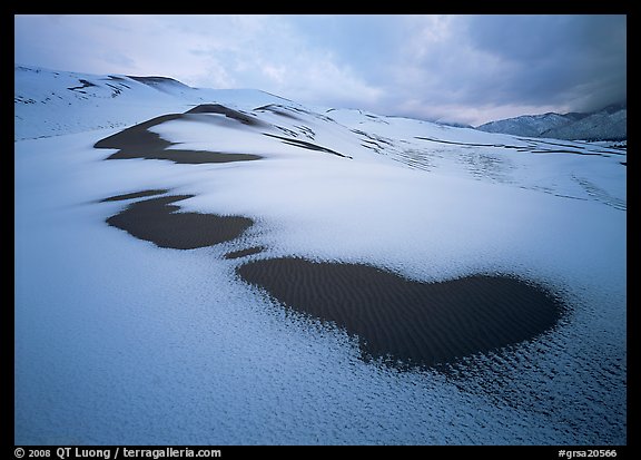 Patches of uncovered sand in snow-covered dunes, mountains, and dark clouds. Great Sand Dunes National Park and Preserve (color)